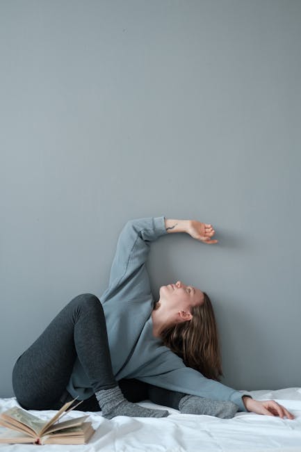 Person in casual clothes sitting in a meditation pose on a mat in a home environment.